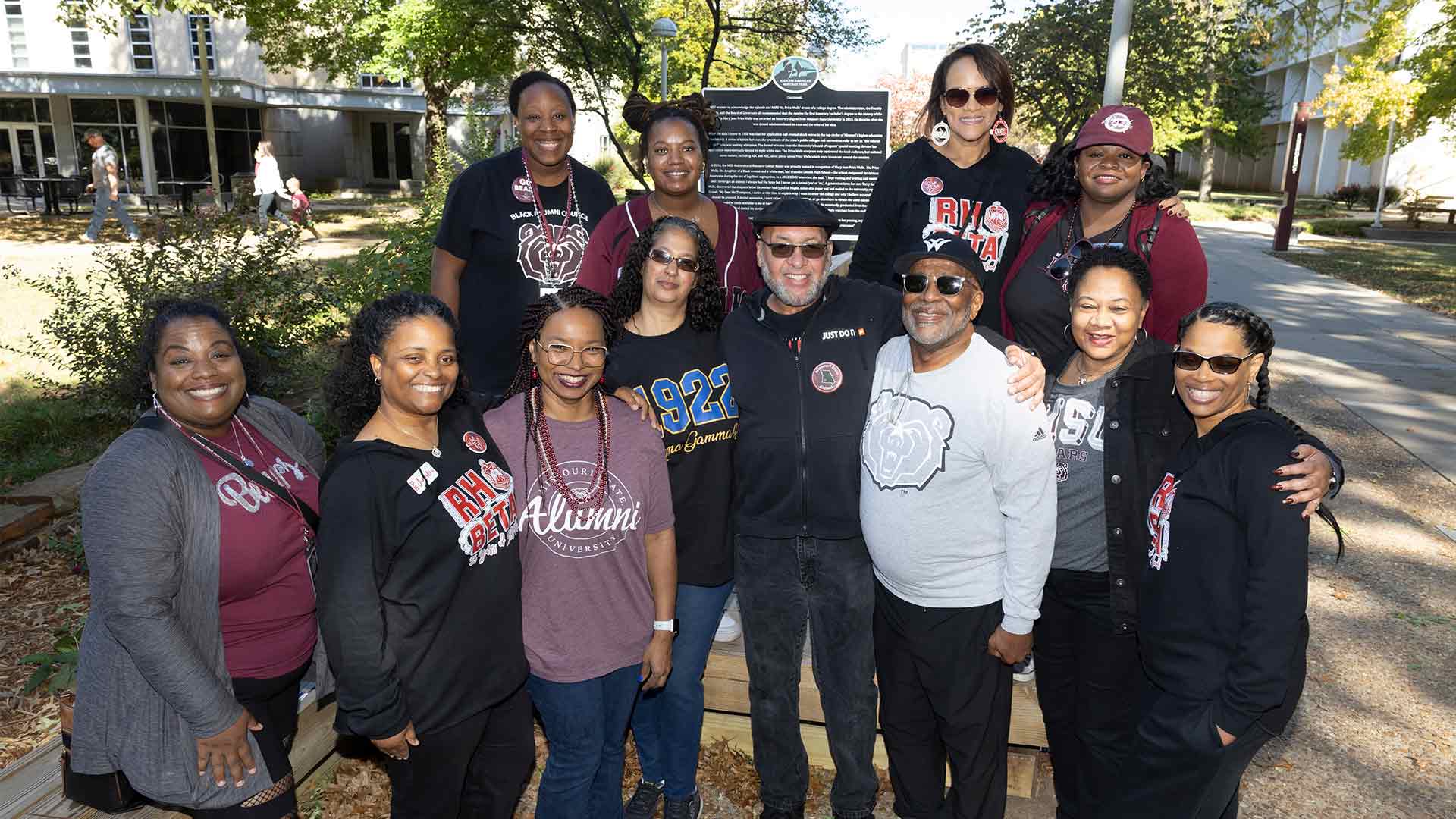 A group of Black alumni pose together in front of the African-American Heritage Trail marker near Plaster Student Union during Homecoming.