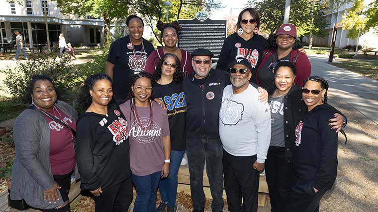 A group of Black alumni pose together in front of the African-American Heritage Trail marker near Plaster Student Union during Homecoming.