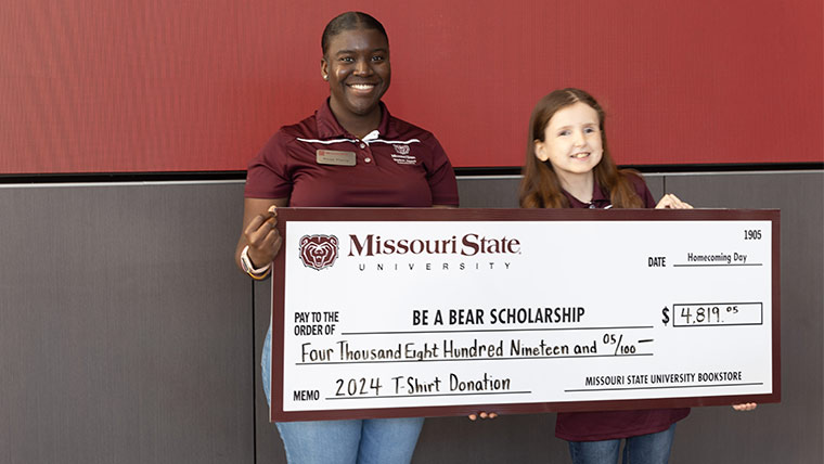 A Student Alumni Association member and a young girl happily hold up a large check for over $4,000 for funds raised during the Be A Bear contest.
