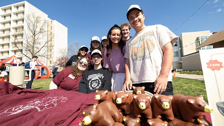 A group of student attendees at the university birthday party on campus. Merchandise can be seen on a table in the foreground.