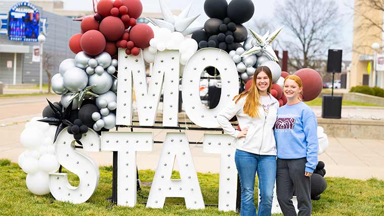 Two students pose for a photo in front of a "Mo State" sign at the university birthday party on campus.