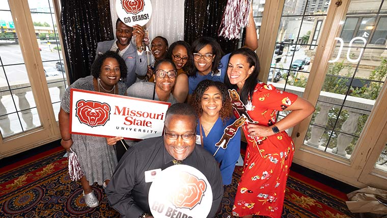 A group of alumni holding up Missouri State signs and posters at an alumni event in St. Louis.