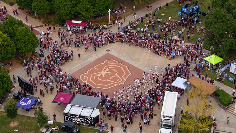 An aerial view of fans and cheerleaders gathered around the maroon Bear head along on the west mall during a pregame tailgate.