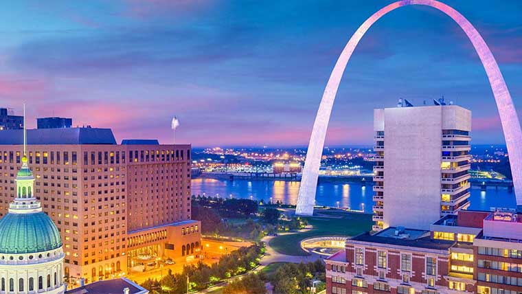 Buildings and the Arch lit up in downtown St. Louis during early evening.
